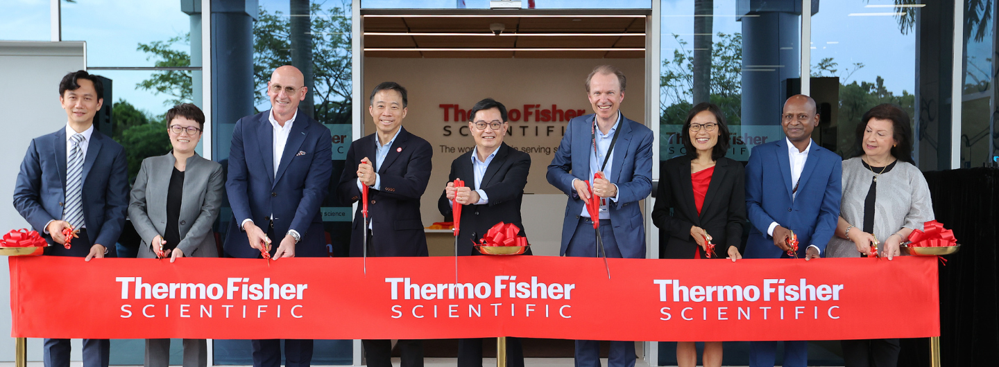 People cutting red "Thermo Fisher SCIENTIFIC" ribbon with scissors at a building entrance.